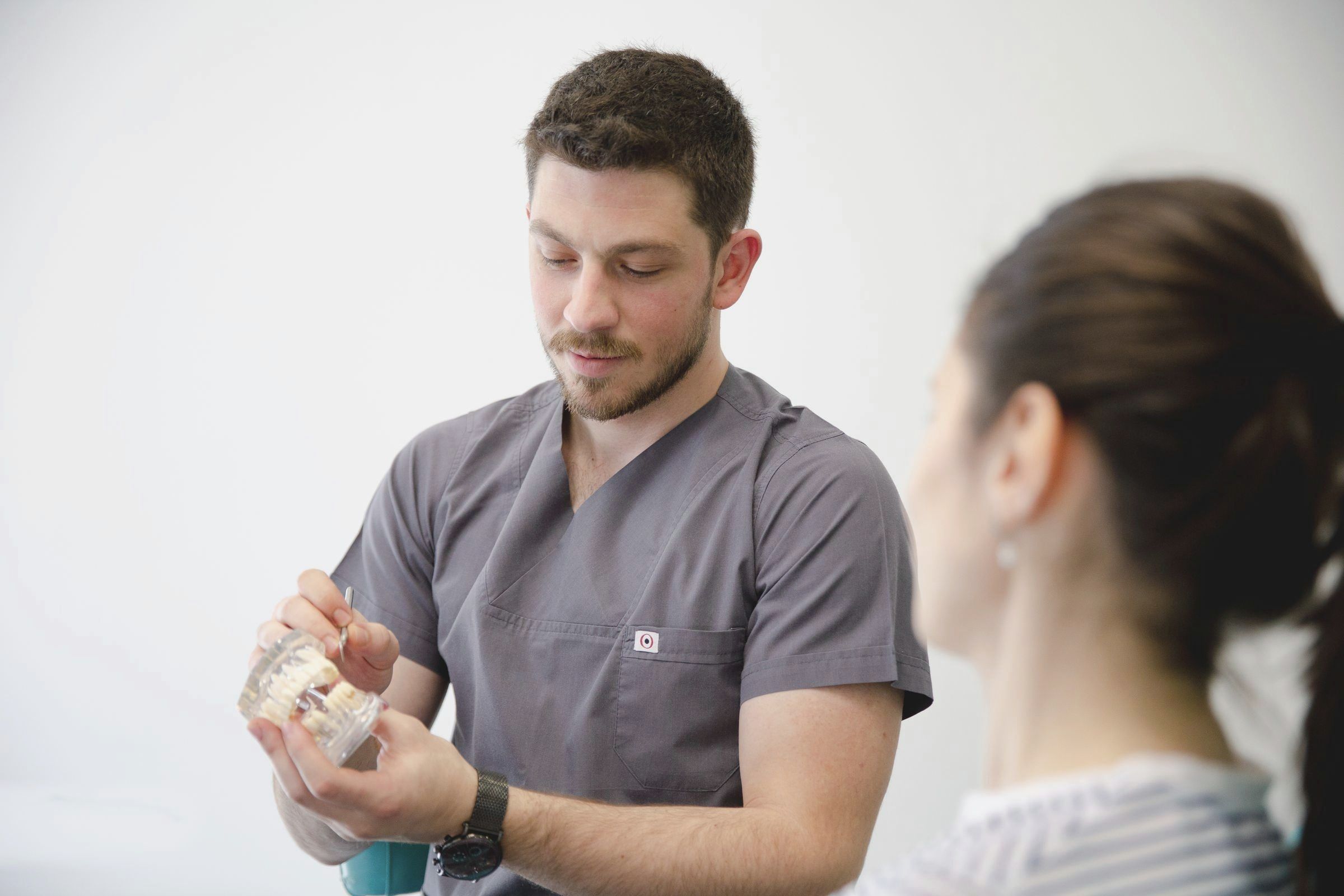 Zahnarzt erklärt einer Patientin an einem Kiefermodell, wie ein Implantat sitzt