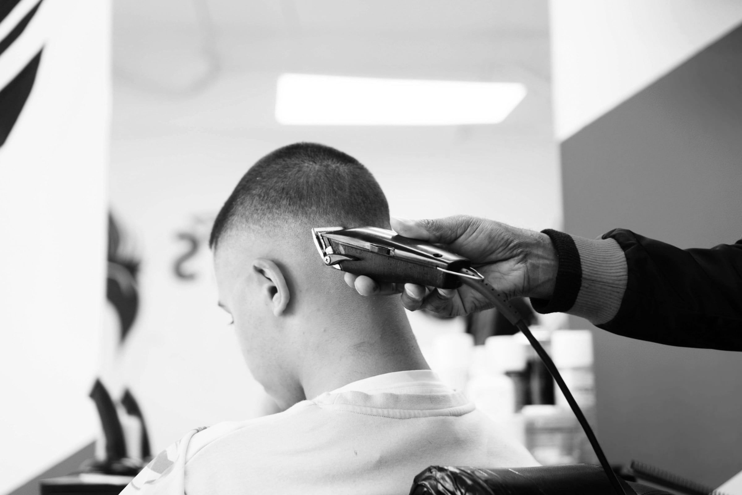 Junge von hinten auf dem Barberstuhl, eine Haarschneidemaschine arbeitet am Hinterkopf